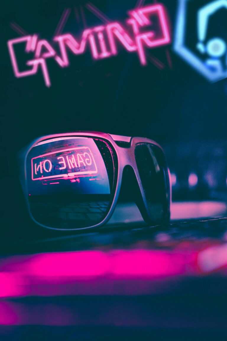 Stylish sunglasses placed on keyboard in dark gaming club with colorful neon illumination